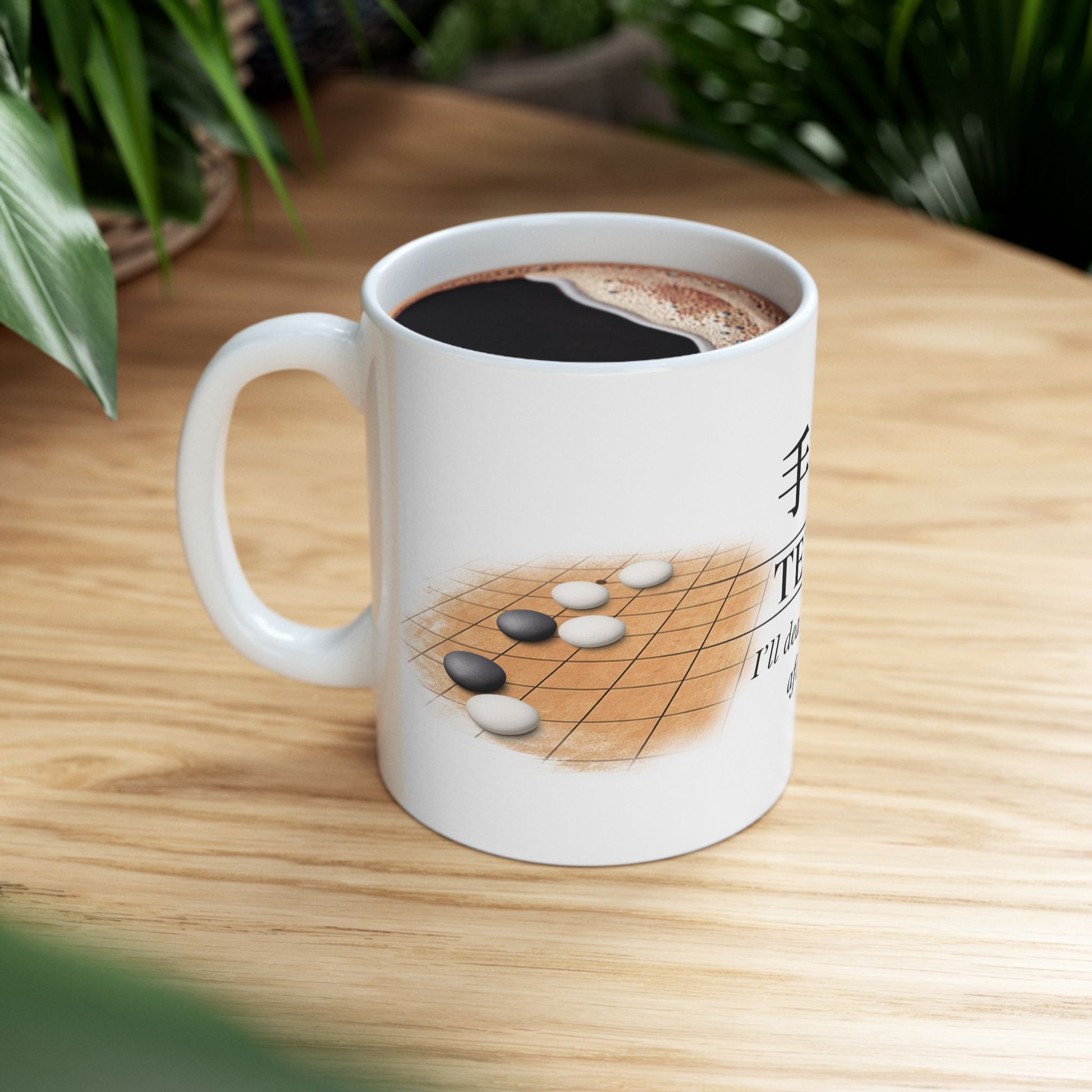 White mug with a design of stones on a game board, filled with coffee, on a wooden surface.