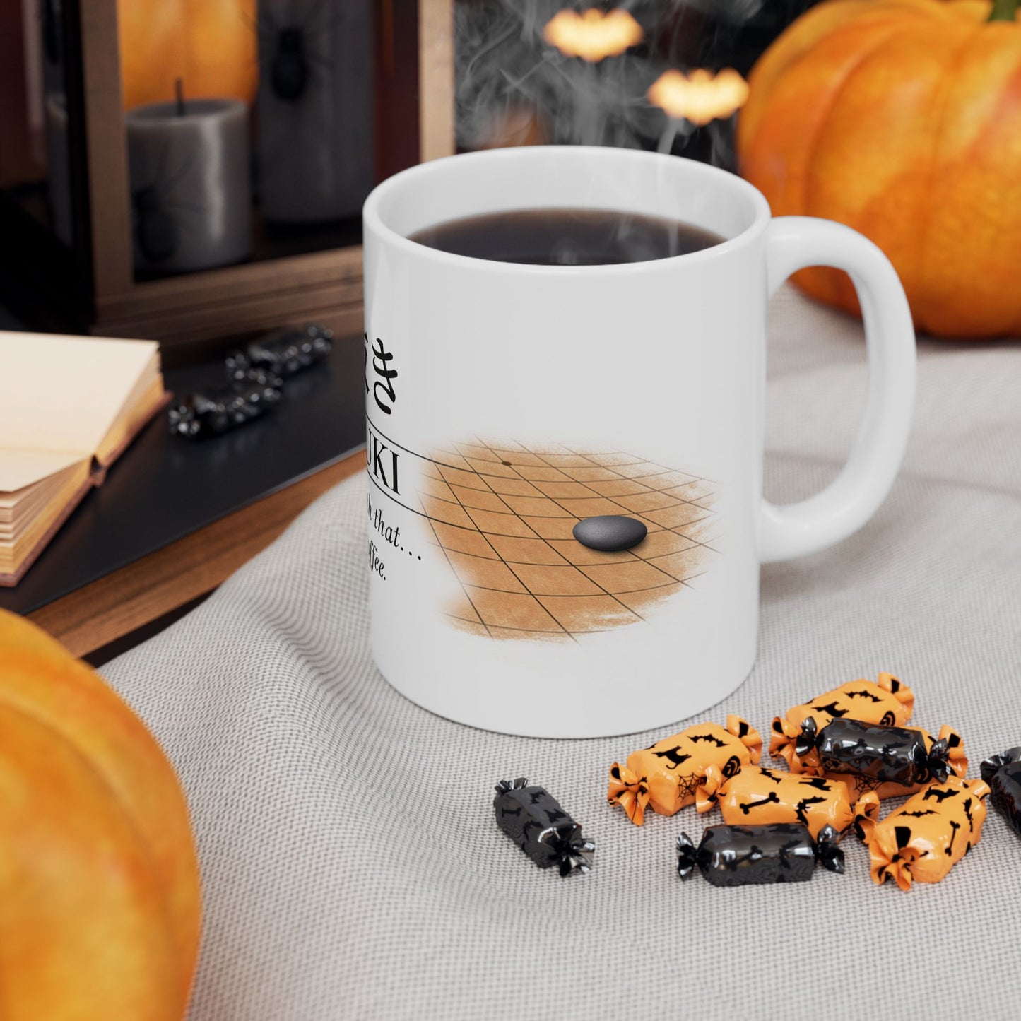 White mug with a design of a chessboard and pieces, filled with a dark liquid, on a table with Halloween-themed treats and pumpkins.